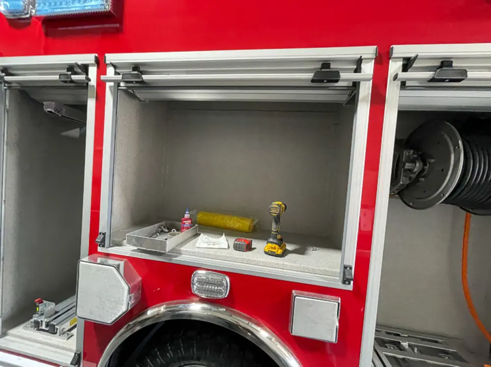 Exterior view of small fire truck showing cab, body compartments, and wheel/tire area.